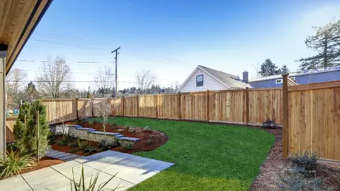 New backyard border bed running along a wooden fence with fresh lawn