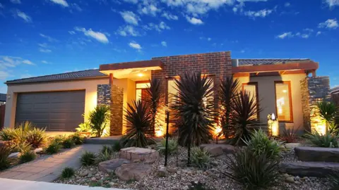 Low-water rock front yard with accent plants and landscape lighting at dusk