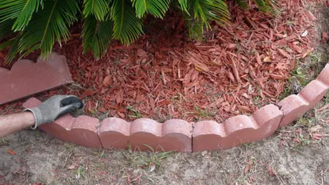 Scalloped red paver edging around a bed of red mulch